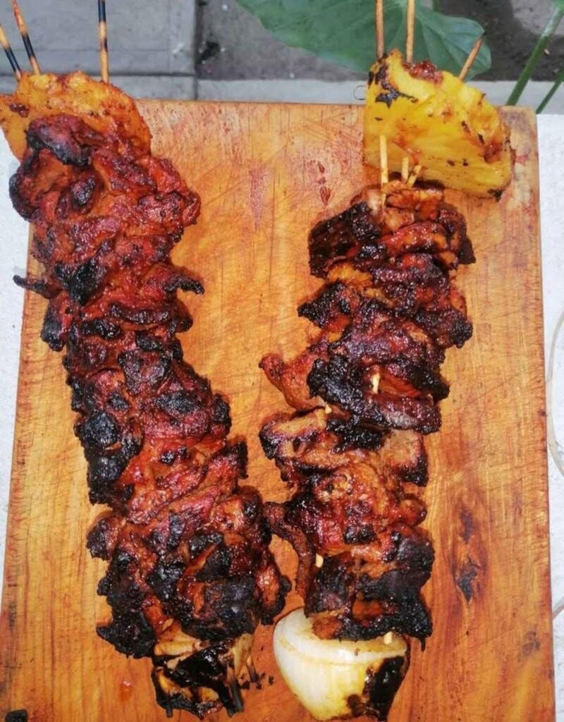 Brochetas de carne al pastor con piña y cebolla sobre una tabla de madera